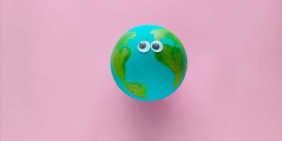 Earth planet model with googly eyes on a pastel pink background