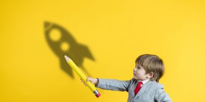 Happy child holding pencil against yellow background